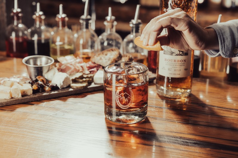 A person squeezing a orange rind into an old fashioned. 