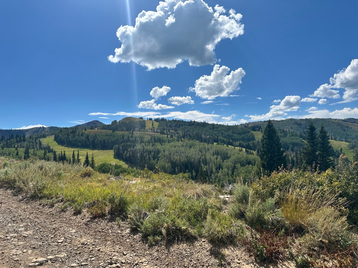 Lush landscape of Park City Utah in the summertime with a ray of sunshine and white puffy clouds.